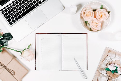 Currently Obsessed - flatlay of journal with pen, flowers ,and laptop